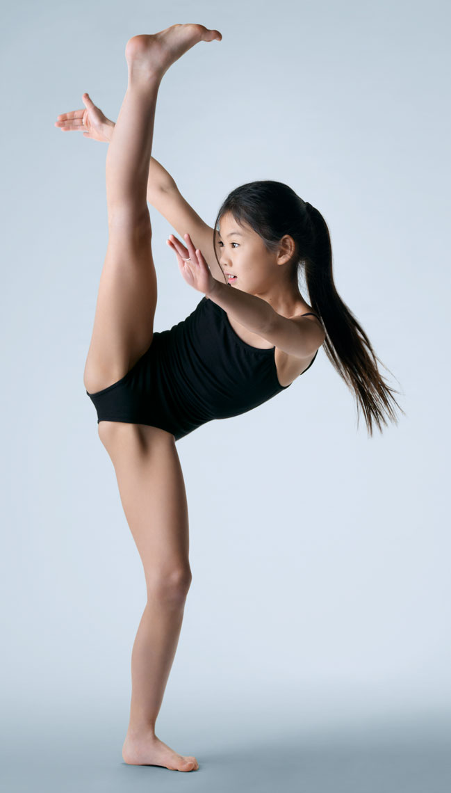 Color child portrait in the studio of a young gymnast kicking high above her head