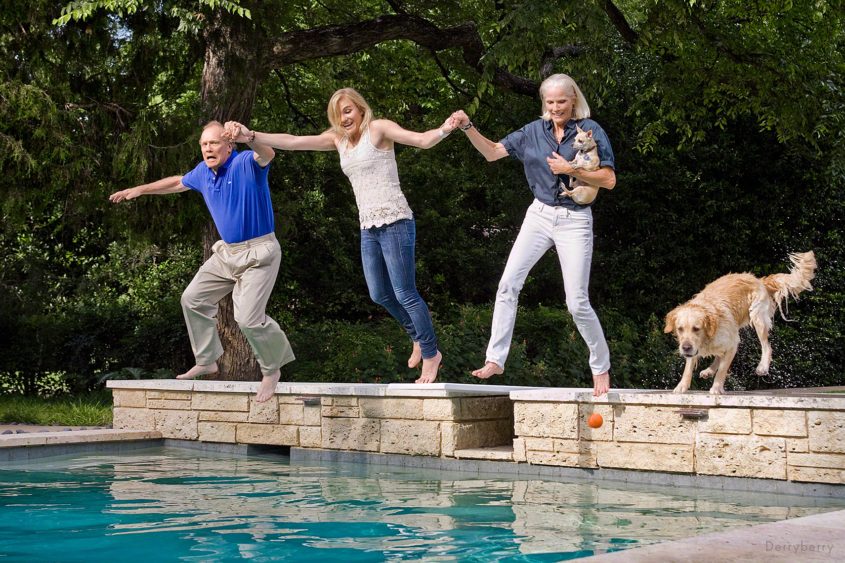 Color portrait of a family holding hands and  jumping into their swimming poo l with their dogslin Dallas, Texas by photographer John Derryberry Photography