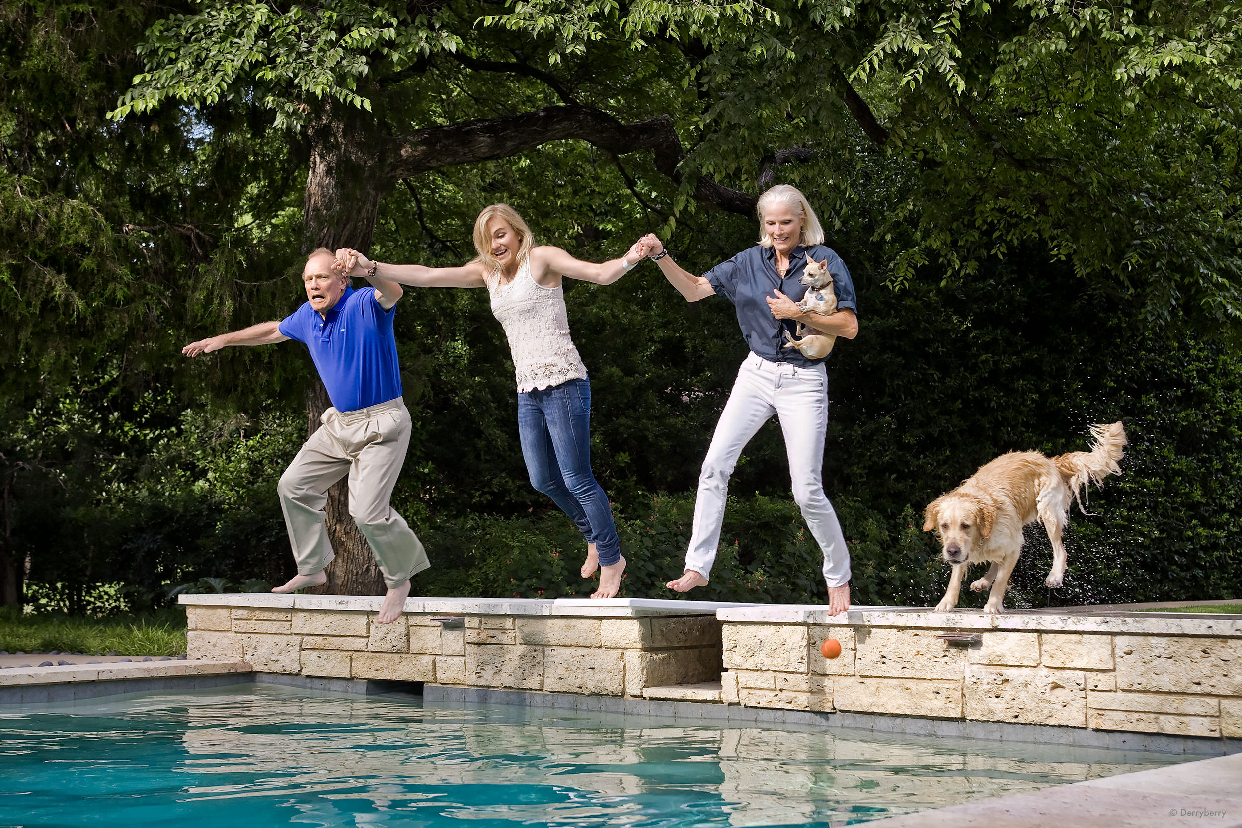 Color location portrait of the Stool family holding hands and jumping in the pool with their dogs