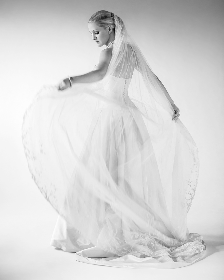 Black and white studio bridal portrait of bride spinning and holding her veil