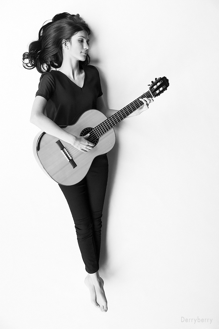 Black and white senior portrait of Maya Muralidhar with her guitar, lying on the floor in the studio  in Dallas, Texas by photographer John Derryberry Photography