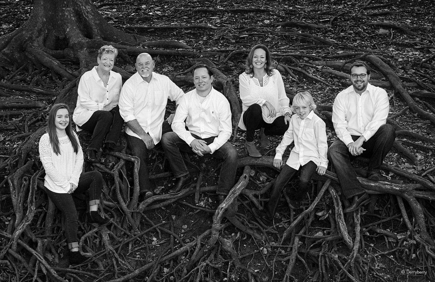 Black and white location group portrait of the Sowden extended family sitting in roots by a creek in Highland Park, Texas  by photographer John Derryberry Photography 