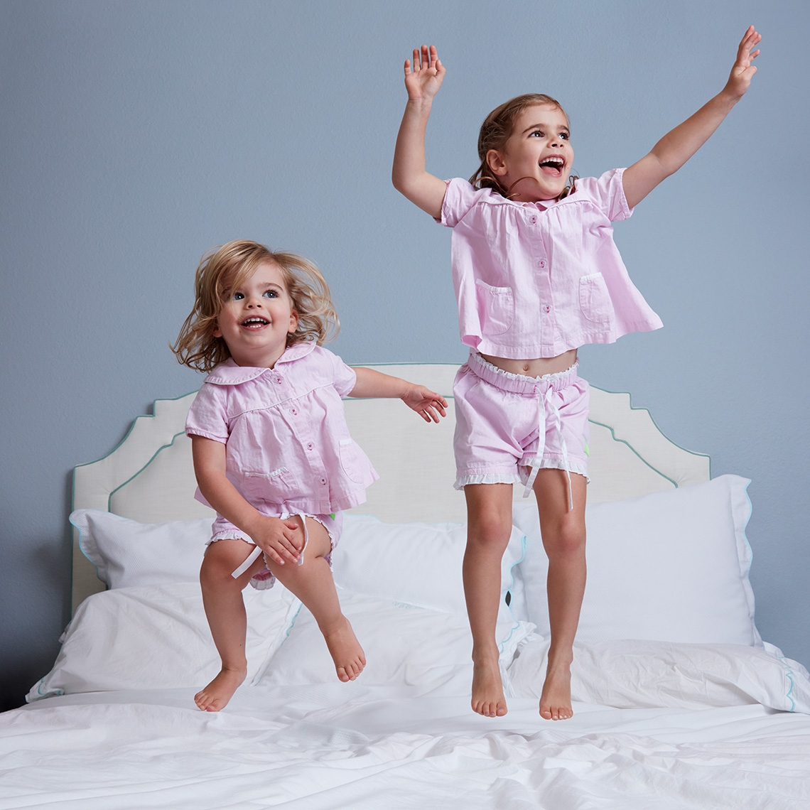 Color portrait of two little sisters in their pajamas jumping on their parent
