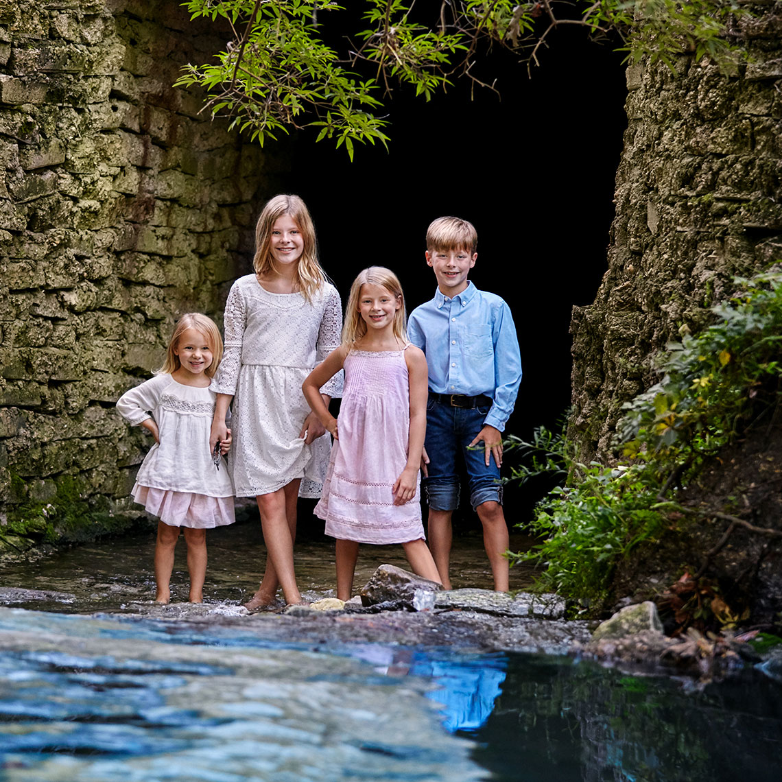 Color portrait of four, bare foot children in a creek by a cave by in Highland Park, Texas by John Derryberry