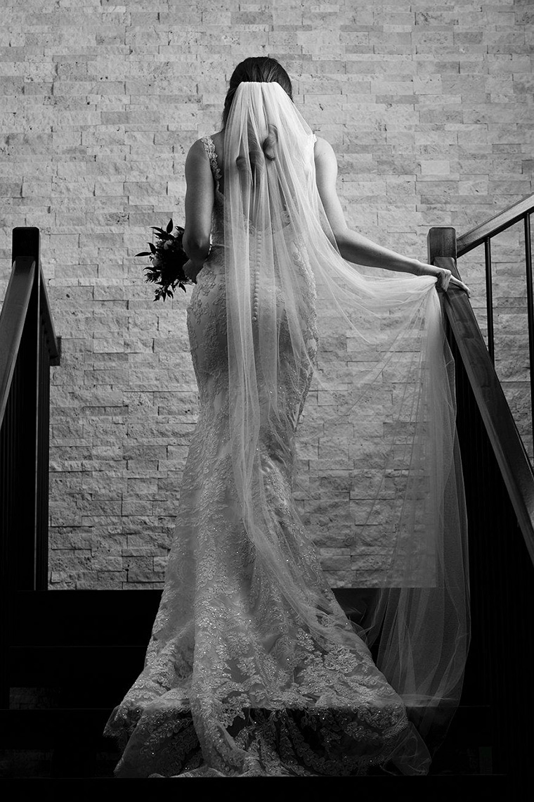 Black and white bridal portrait of a bride walking up stairs while holding her veil