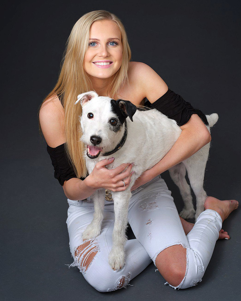 Color studio senior portrait of Anna Disney with her dog, sitting on the floor in the studio  in Dallas, Texas by photographer John Derryberry Photography