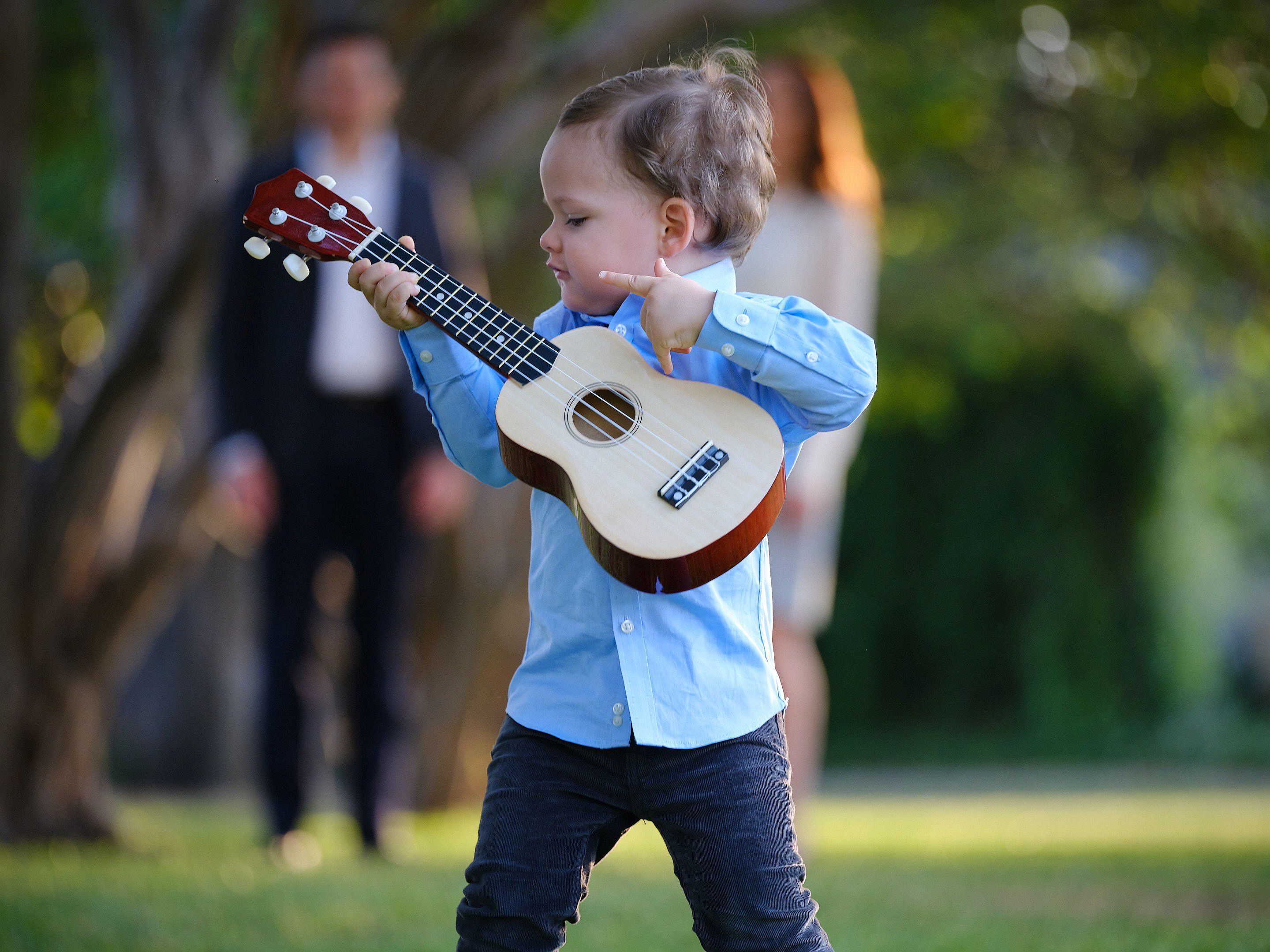 Color location portrait of a little boy playing a small guitar with his parents watching behind him