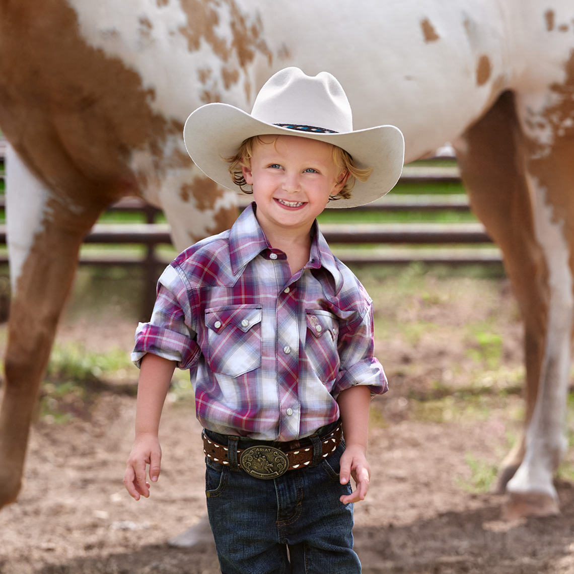 Color portrait of a little cowboy in a white hat with an appaloosa horse behind him at South Fork Ranch, in Dallas, Texas  by john Derryberry