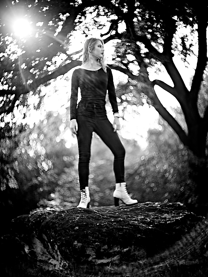 Black and white  bokeh senior Portrait of Becca Hain wearing white boots and using a vintage Zeiss Prokinar 140mm projection lens in a park  in Dallas, Texas by photographer John Derryberry Photography