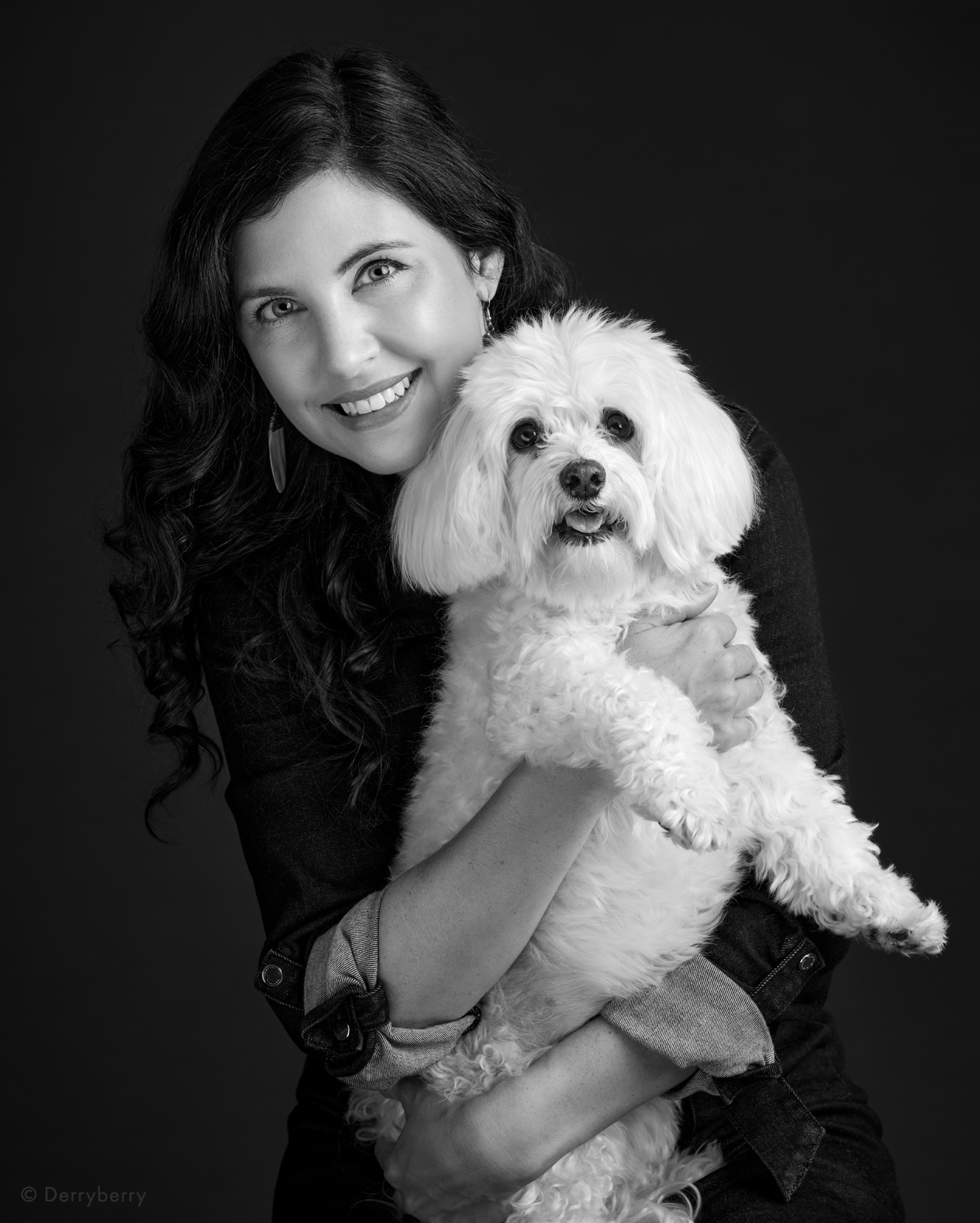 Professional b&w studio portrait shot against a dark background of a smiling woman holding her sweet family pet