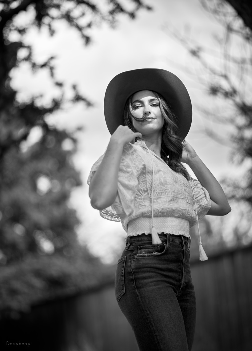 B&W photograph of young woman in cowboy hat and blue jeans outdoors