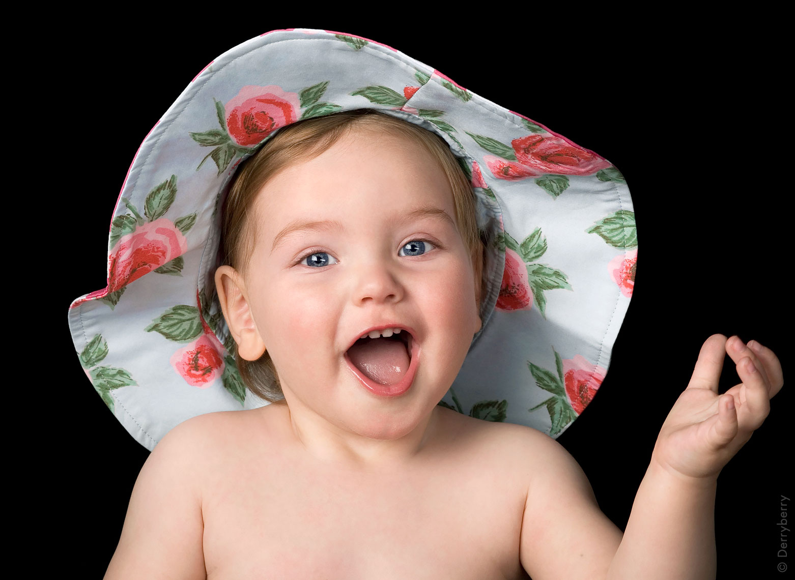 Portrait of a pretty and happy baby girl with a flowered hat on holding her hand up